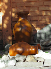 Orange Clay Handmade Vase with White Stones on Gray Cement Wall in Garden Sunny Green Orange in Summer