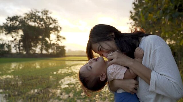 happy mother carry her baby playing together outdoor enjoy beautiful sunset in the field