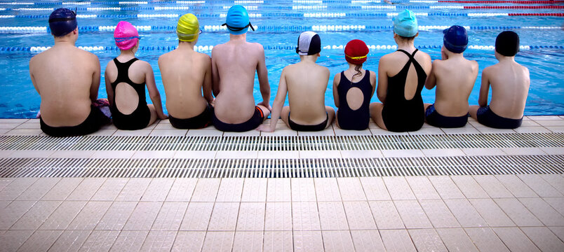 Back view of a group of happy young children wearing swimwear sitting at the swimming pool - Powered by Adobe
