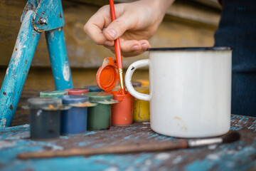 Multi-colored gouache and enameled mug on an old ragged stand