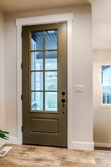 Hinged front door with glass pane viewed from interior of home with wood floor