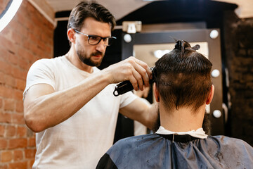 Young handsome barber making haircut of attractive man in barbershop