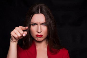 Emotional head shot portrait of a brunette caucasian woman in red dress and with red lips on black...