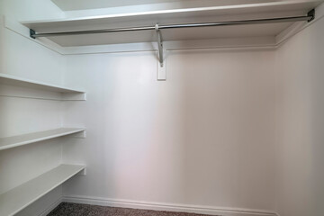 Empty walk in closet of new home with wall shelves and hanging clothes rod