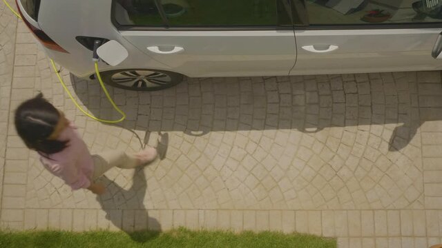 High angle shot of a woman plugging the eco-friendly electric car to charge on her backyard