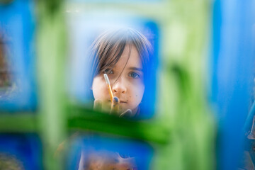 A boy in a red T-shirt draws with colorful gouache on the window