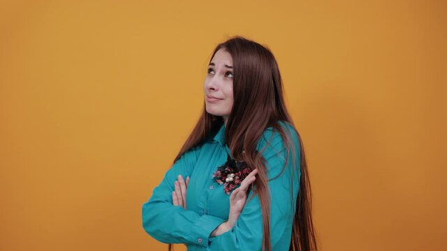 Standing and cross her arms on chest. Young attractive woman with brown hair and eyes, decoration on blue shirt, yellow background