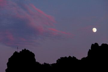 The silhouette of moon over the rocky hill. Reddish clouds are up on the sky leaning towards the...