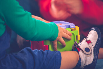 Baby boy is playing with cubic colorful toy. Childhood and friendship. Girl is out of focus in the background. Colourful toy and children playing with those toys. Cute boy wears cute shoe.