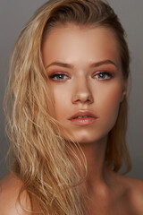 Closeup face fashion beauty portrait of young beautiful caucasian blonde woman with wet hair and makeup posing against gray background.