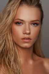 Fototapeta premium Closeup face fashion beauty portrait of young beautiful caucasian blonde woman with wet hair and makeup posing against gray background.