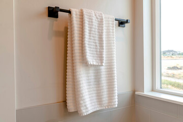 Black rod with white towel mounted on the bathroom wall with tiles