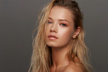 Naklejka premium Closeup face fashion beauty portrait of young beautiful caucasian blonde woman with wet hair and makeup posing against gray background.