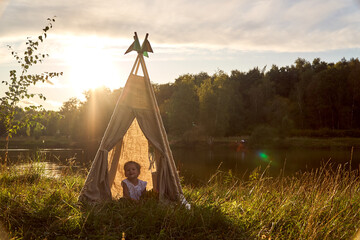 A little girl is sitting by the lake. Sunny akat. Wigwam. Happy child. High quality photo