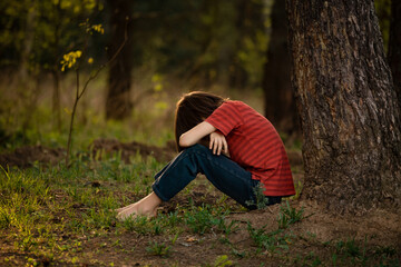 A boy in a red T-shirt sits on the grass in the sunshine
