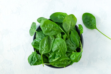 Fresh spinach leaves in a black bowl on a light surface. Fresh greens. Vegetarianism, healthy eating concept. Horizontal orientation, selective focus. View from above.