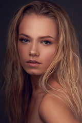 Obraz premium Closeup face portrait of young pretty caucasian woman with long blonde woman looking in camera and posing against gray background. Shallow DOF.