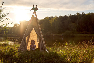 A little girl is sitting by the lake. Sunny akat. Wigwam. Happy child. High quality photo