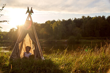 A little girl is sitting by the lake. Sunny akat. Wigwam. Happy child. High quality photo