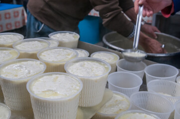 The making of ricotta cheese: farmer filling small plastic containers with hot ricotta cheese