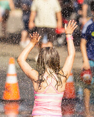 Young girl playing in the water spray at an event with her arms and hands raised up.