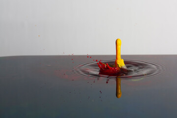 Splash of bright paint in still water. Drop of toxic yellow and red paint falling on calm surface of clean water and causing ripples
