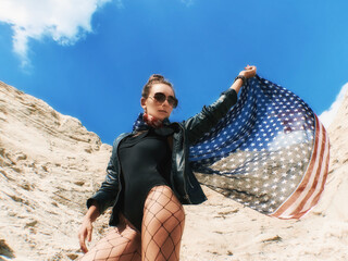 Model Girl holding the american flag and looking ahead in desert. The american flag keeping in the wind. Copy space