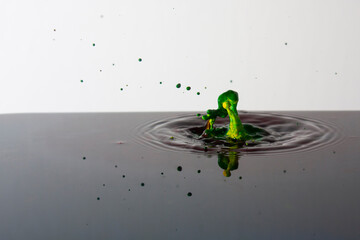 Splash of bright paint in still water. Drop of toxic green and yellow paint falling on calm surface of clean water and causing ripples