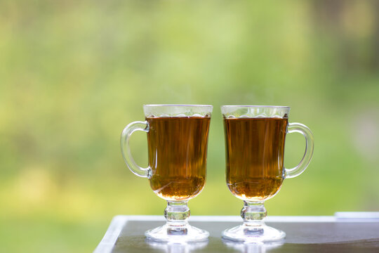 Two beautiful glass glasses with black tea on nature on a natural green background