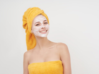 Smiling young woman with cream mask on face with towel on the hair