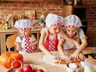 Three little chefs enjoying in the kitchen making cakes. Girls at the kitchen. Family housekeeping.