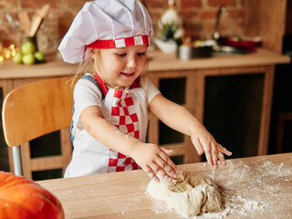 Little girl in cooking chef clothes enjoys kneading the dough. Girls at the kitchen. Family housekeeping.