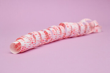 measuring tape is laid out diagonally on a blurred background of lilac paper. the concept of weight loss.