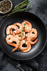 Cooked peeled king prawns, shrimps on a plate. Black background. Top view