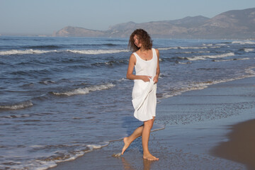 A smiling happy woman in white dress walking near a beach in hot sunny summer day. High quality photo