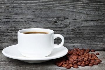 A cup of coffee and coffee beans on a wooden background. Heap of coffee beans. White coffee cup and saucer.Copy space. Place for text.