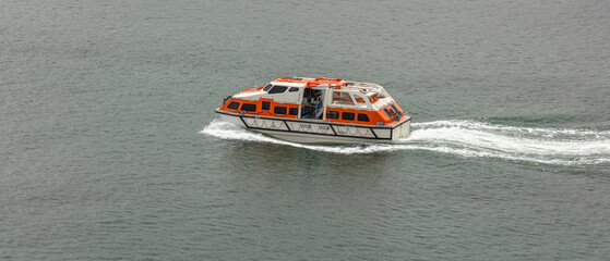 Orange-and-white life boat moving fast in the water. Life saving equipment concept. 