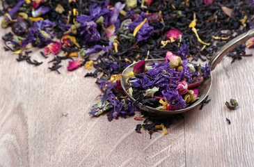 blended black tea in a spoon with flower petals on a wooden table. copy space