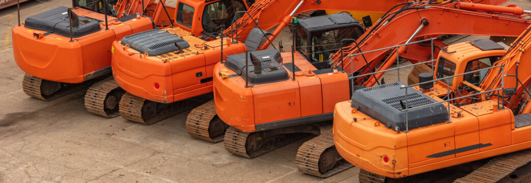 Old orange heavy excavators parked in one row on concrete surface. Construction site. Aerial angled view.