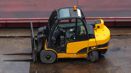 Yellow forklift parked on wet concrete surface. Industrial site. © Sergey