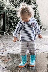 petite fille joue dans une flaque d'eau avec ses bottes