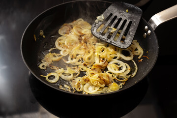 Onions are roasted in a black pan on a modern stove, selected focus, narrow depth of field