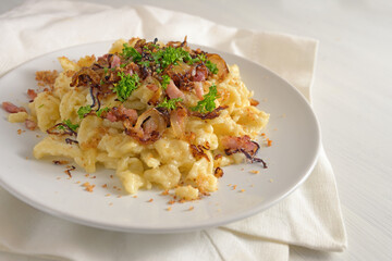 Homemade German egg pasta, called spaetzle, with cheese, roasted bacon, onion and breadcrumbs on a white painted wooden table, traditional in southern Germany and Austria, copy space, selected focus