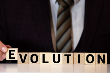 Close-up Of Person's Hand Placing Last Alphabet Of Word Evolve On Wooden Block