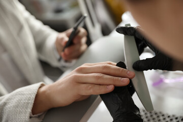 Professional manicurist filing client's nails in beauty salon, closeup