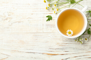 Cup of tea and chamomile flowers on white wooden table, flat lay. Space for text