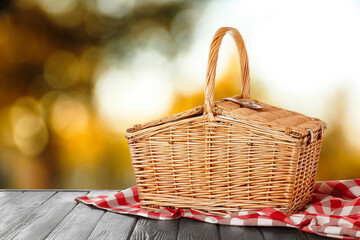 Wicker picnic basket on wooden table outdoors, space for text