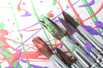 Brushes on canvas with colorful paint splashes, closeup. Art and creativity