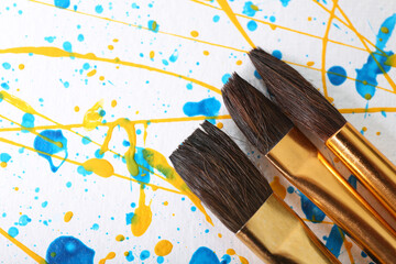 Brushes on canvas with colorful paint splashes, closeup. Art and creativity