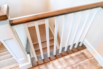 Looking down on U shaped indoor staircase with white baluster and brown handrail